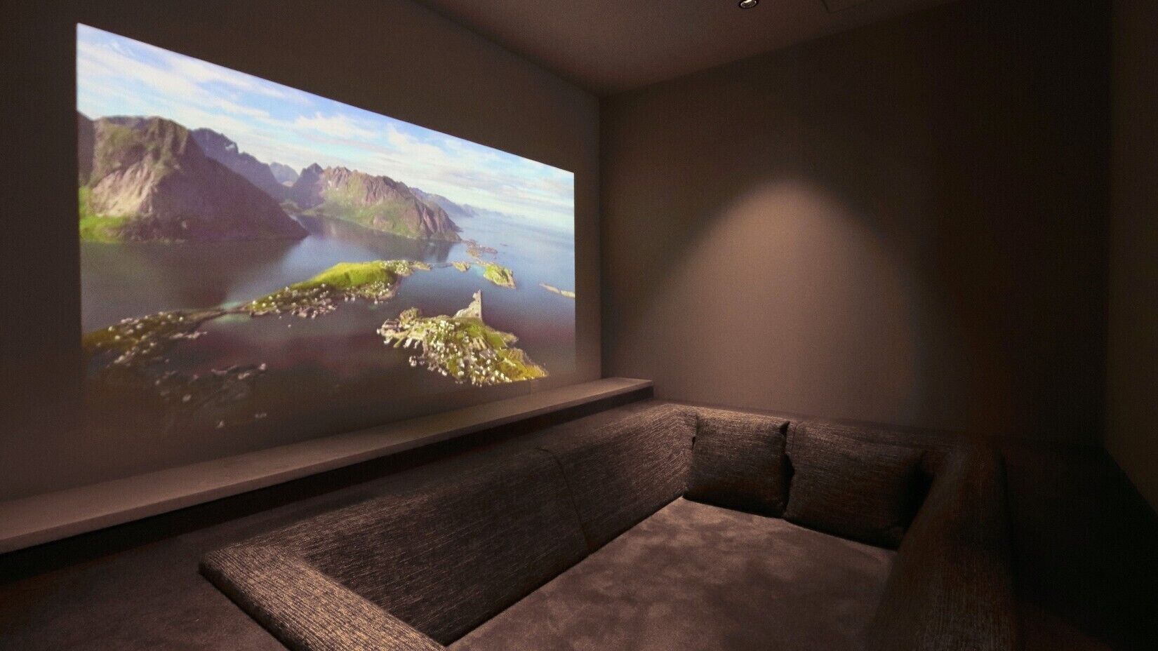 A room with a large screen displaying a scenic landscape, a dark-colored sofa, and a wall-mounted shelf.