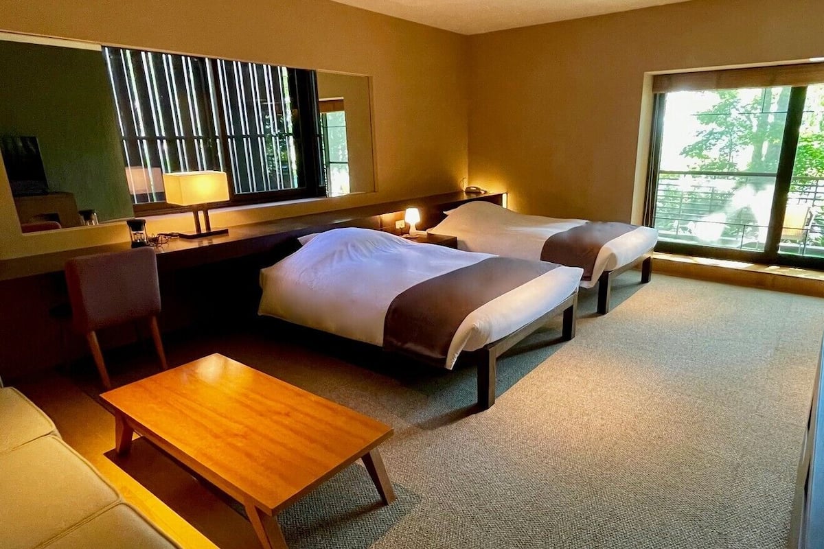 Habitación de hotel con dos camas, un escritorio, una silla, una lámpara y un ventanal con vistas.