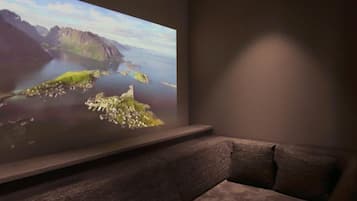 A room with a large flat-screen TV mounted on a wall, a dark-colored sofa, and a small table in front of the TV.