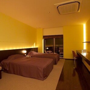 Habitación de hotel con dos camas, un escritorio, una silla y un ventanal grande.