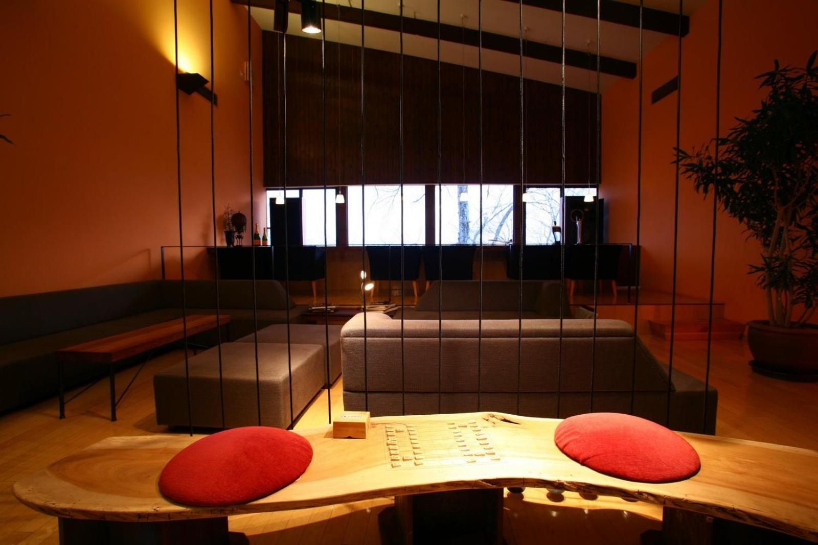 A modern interior with a sofa, a wooden table with red cushions, and a large window providing natural light.