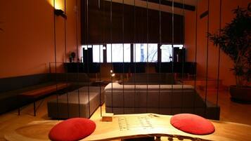 A modern interior with a sofa, a wooden table with red cushions, and a large window providing natural light.