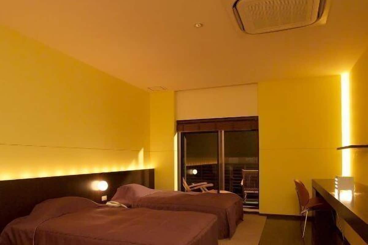 Habitación de hotel con dos camas, un escritorio, una silla y un ventanal grande.