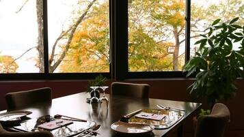 A dining table set for four with chairs, a potted plant, and a window with autumn foliage view.