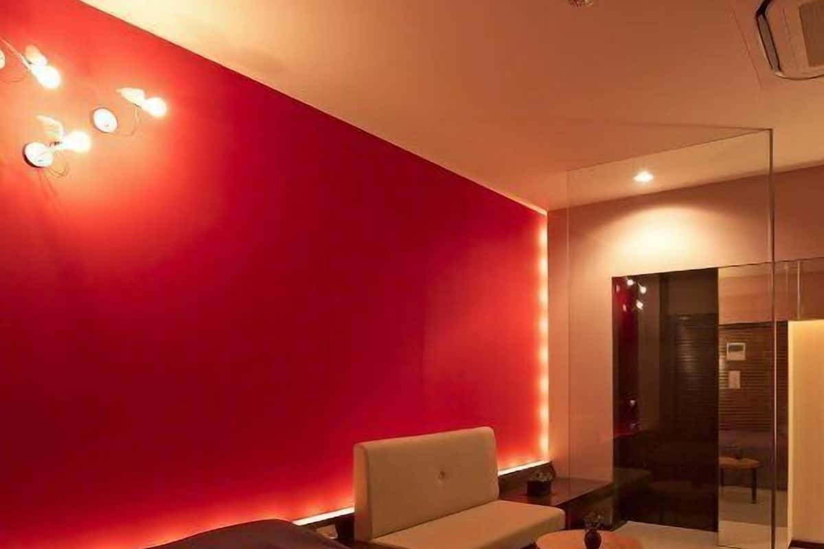 Una habitación de hotel moderna con una pared de acento roja, un sofá, una mesita y un separador de vidrio.