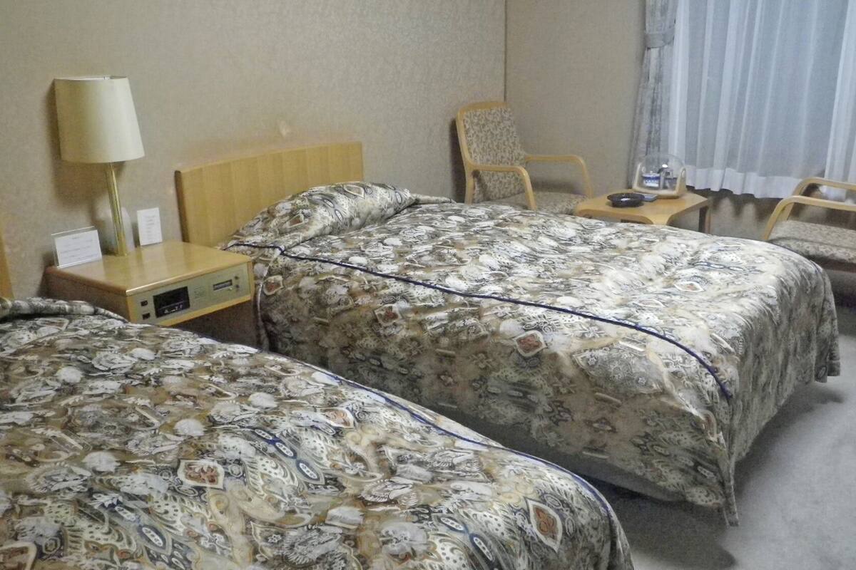 A hotel room with two beds, a desk, a chair, a lamp, and a window with curtains.