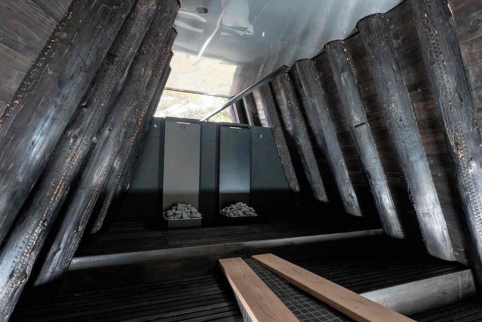 Espacio estrecho y cerrado con paredes de metal y techo inclinado, que presenta un banco metálico central y dos cajas metálicas en el suelo.