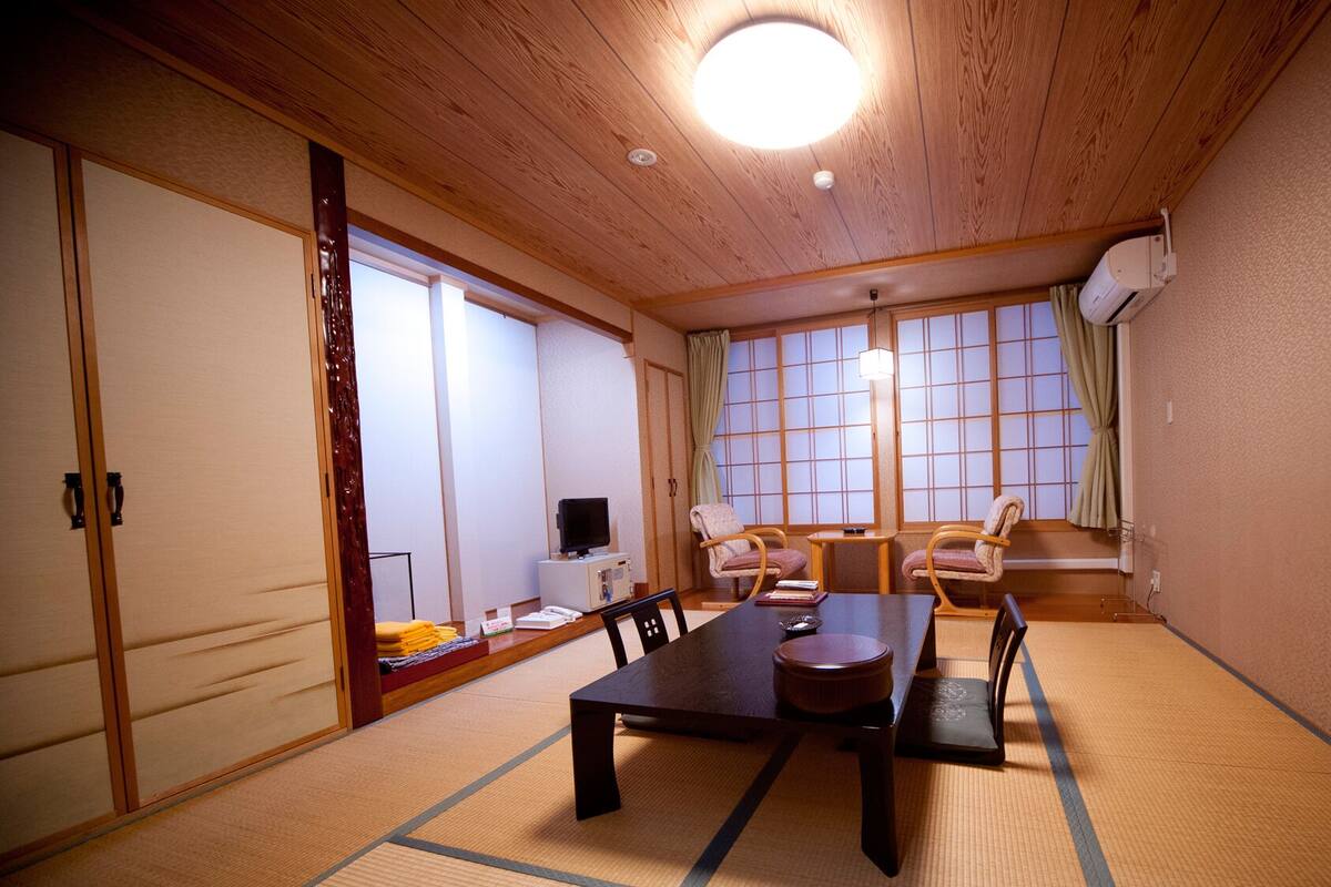 A traditional Japanese room with tatami flooring, a low table, two chairs, a television, and sliding doors.