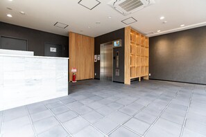 Een receptiezone met een receptiebalie, een brandblusser, een lift en een televisietoestel aan de muur.