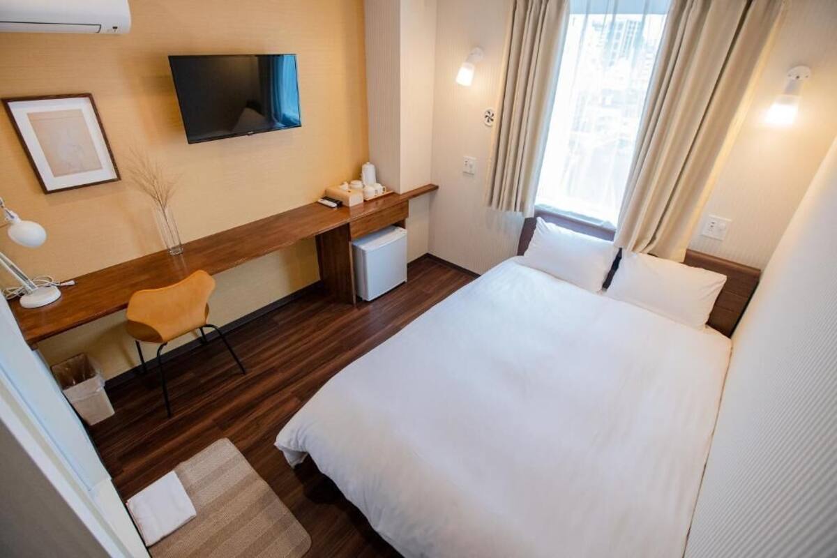 A hotel room with a bed, a desk, a chair, a TV, and a window with curtains.