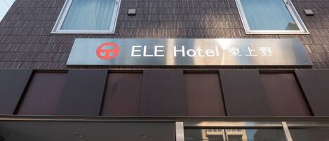 A tall hotel building with a modern design, featuring a prominent logo and signage indicating it is the ELE Hotel.