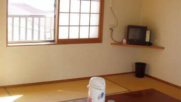 Ein Zimmer mit Tatami-Böden, einem verschiebbaren Shoji-Bildschirm, einem Fernseher auf einem Regal und einem Tisch mit einem Teeset.
