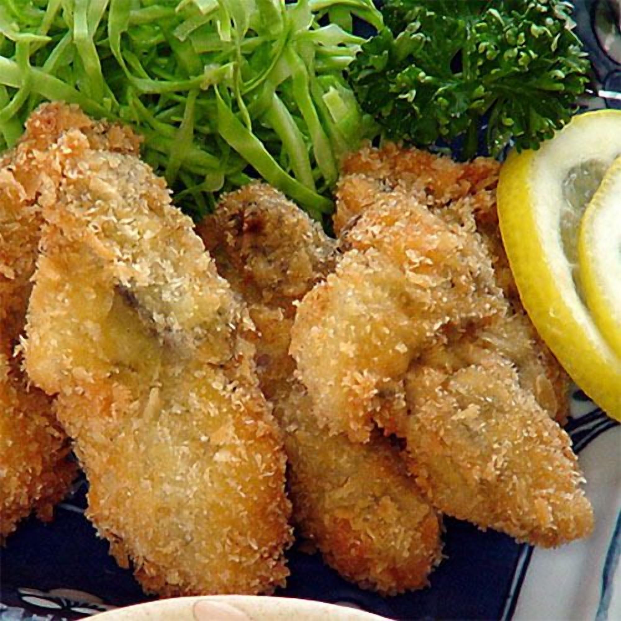 Ein Teller mit paniertem und frittiertem Essen, vermutlich Chicken Nuggets, dazu ein Beilagensalat mit grünen Gemüsesorten und eine Zitronenscheibe.