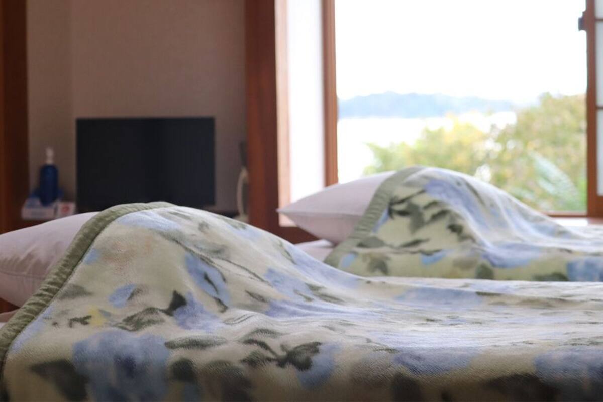 A hotel room with two beds, a television, and a view of the outdoors.