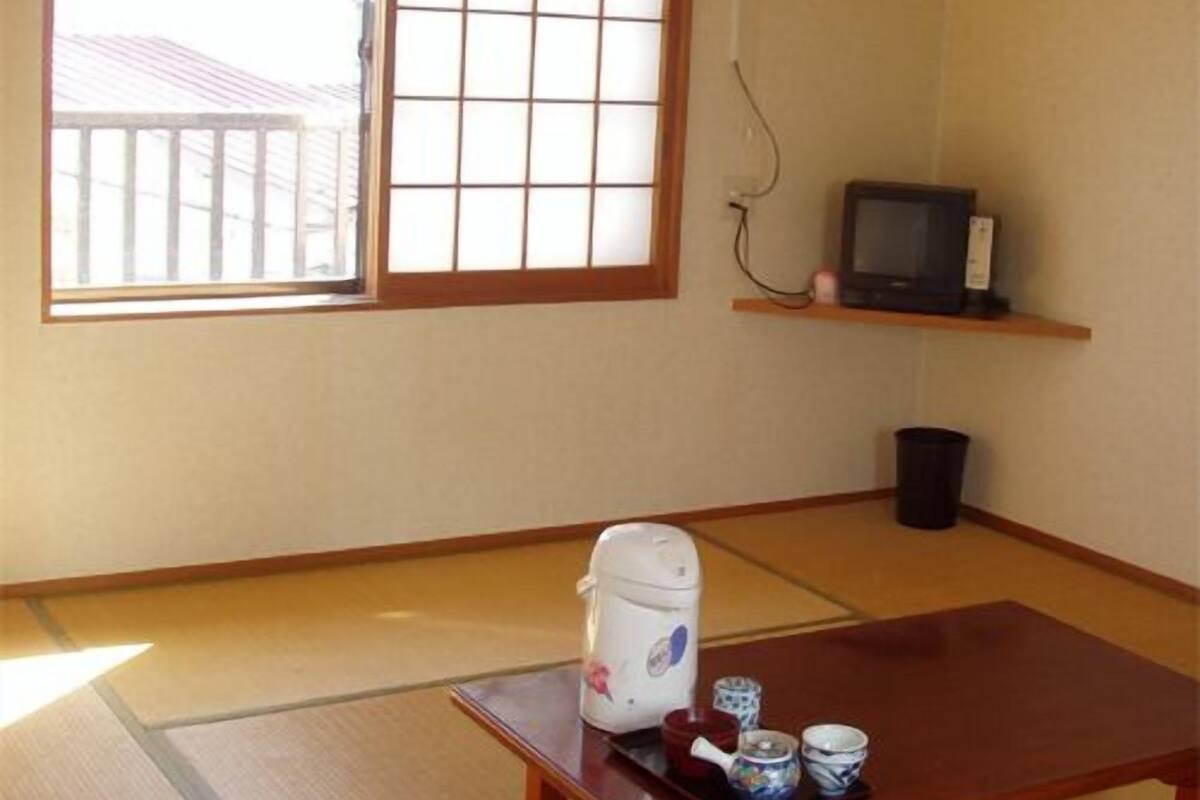 A room with tatami flooring, a sliding shoji screen, a television on a shelf, and a table with a tea set.