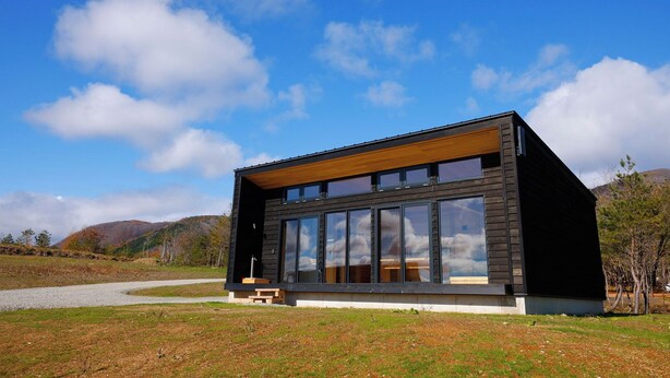 Uma cabana moderna com grandes janelas, um deck de madeira e vista para a paisagem ao redor.