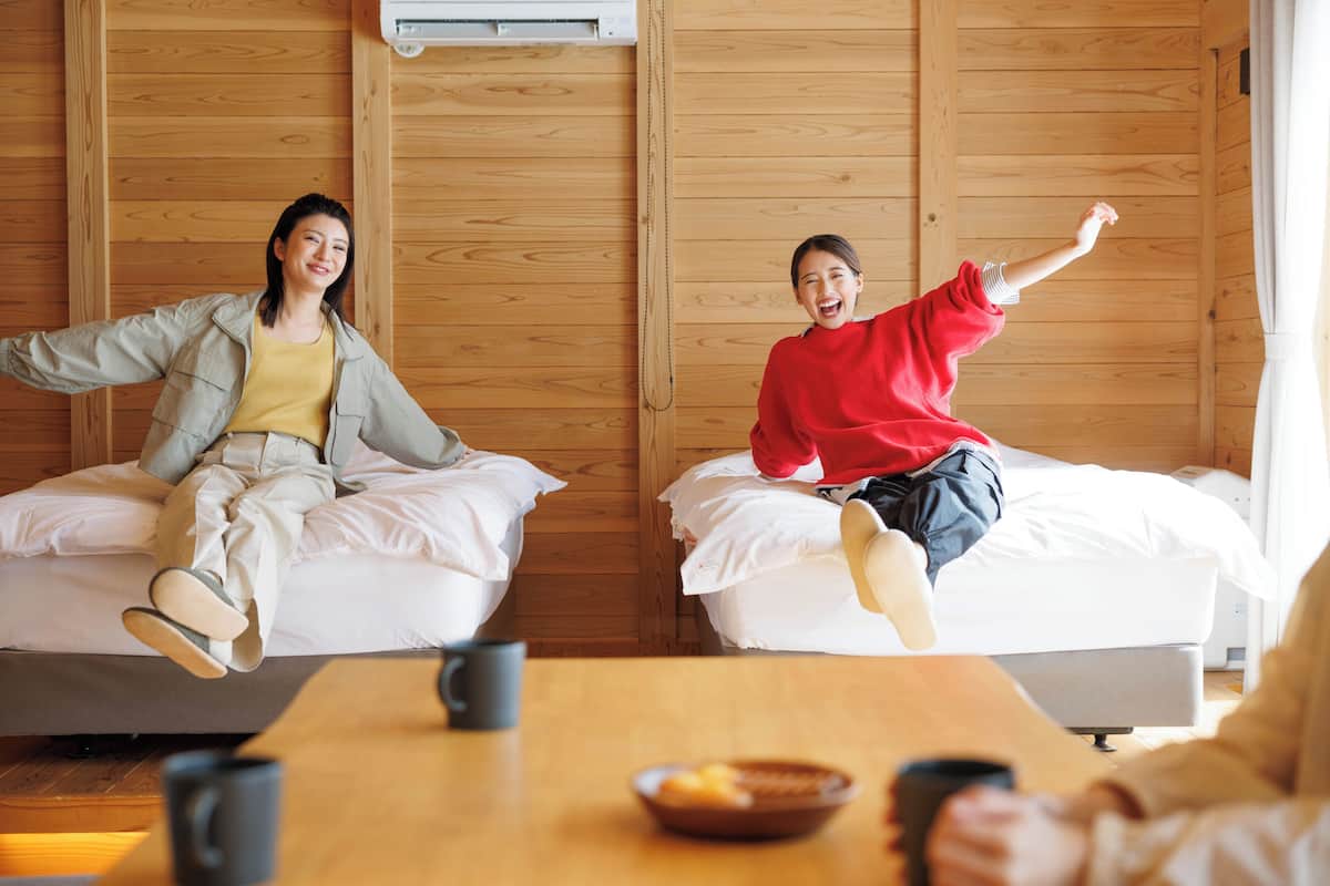 Una habitación con paredes de madera, dos camas, una mesa con un tazón y tazas, y un aire acondicionado.