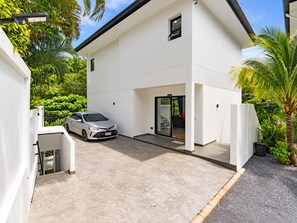 A modern two-story house with a car parked in the driveway, surrounded by lush greenery. - Luxurious Villa With Private Pool and Stunning Views (Chalong)