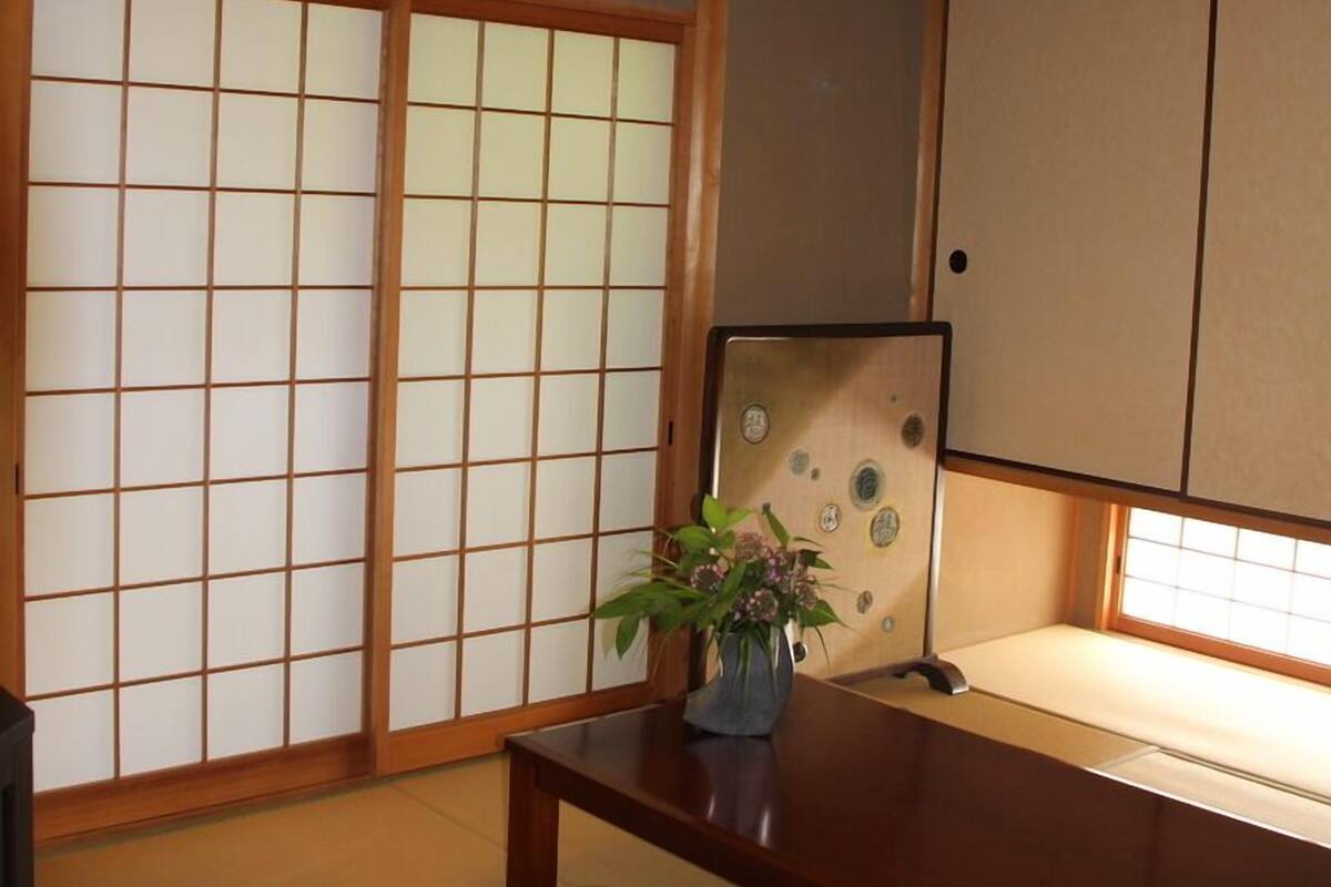 Une pièce de style japonais traditionnel, avec un sol recouvert de tatamis, des portes coulissantes, une petite table en bois et une plante.