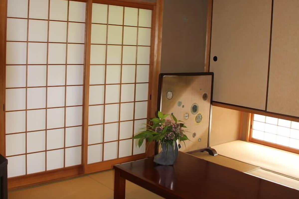 Ein traditioneller japanischer Raum mit Tatami-Boden, Schiebetüren, einem niedrigen Holztisch und einer Pflanze.