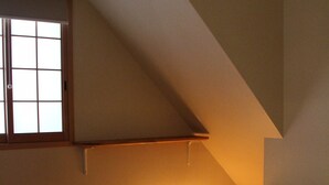 A bedroom with a sloped ceiling, a window with blinds, a bed with a white mattress and a brown blanket, and wooden flooring. - Nishijin Narahian (Kyoto)
