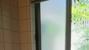 A bathtub with a window above it, tiled walls, and a thermostat on the wall. - Nishijin Narahian (Kyoto)