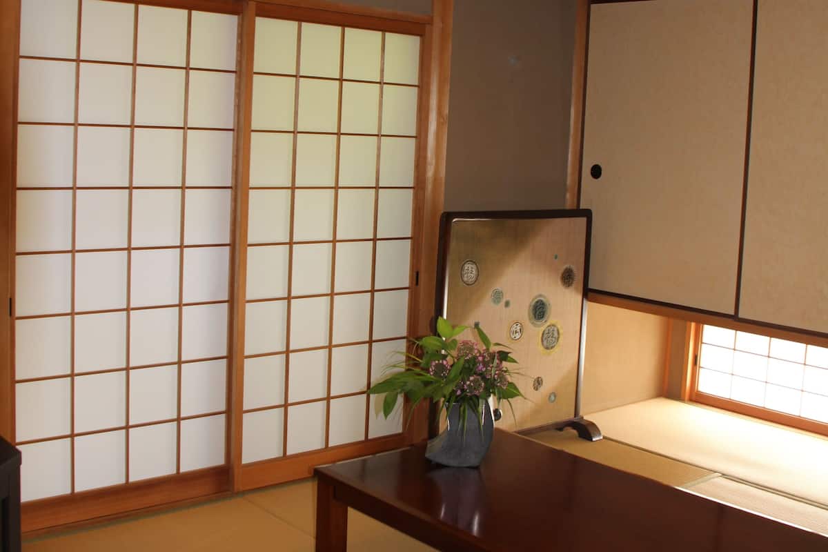 Une pièce de style japonais traditionnel, avec un sol recouvert de tatamis, des portes coulissantes en papier de riz (shoji), une petite table en bois et une plante.