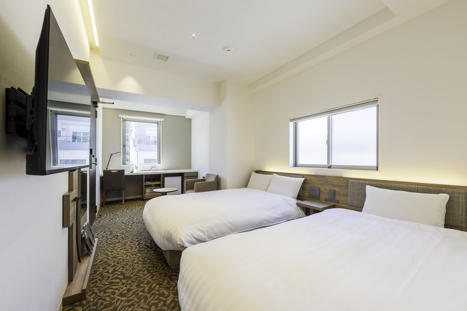 Una habitación de hotel con dos camas, un escritorio, una silla, un televisor y una ventana.