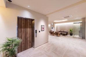 A modern hotel lobby with a wooden elevator, a seating area with a sofa and chairs, and a potted plant. - Tabi And Nagasaki (Nagasaki)