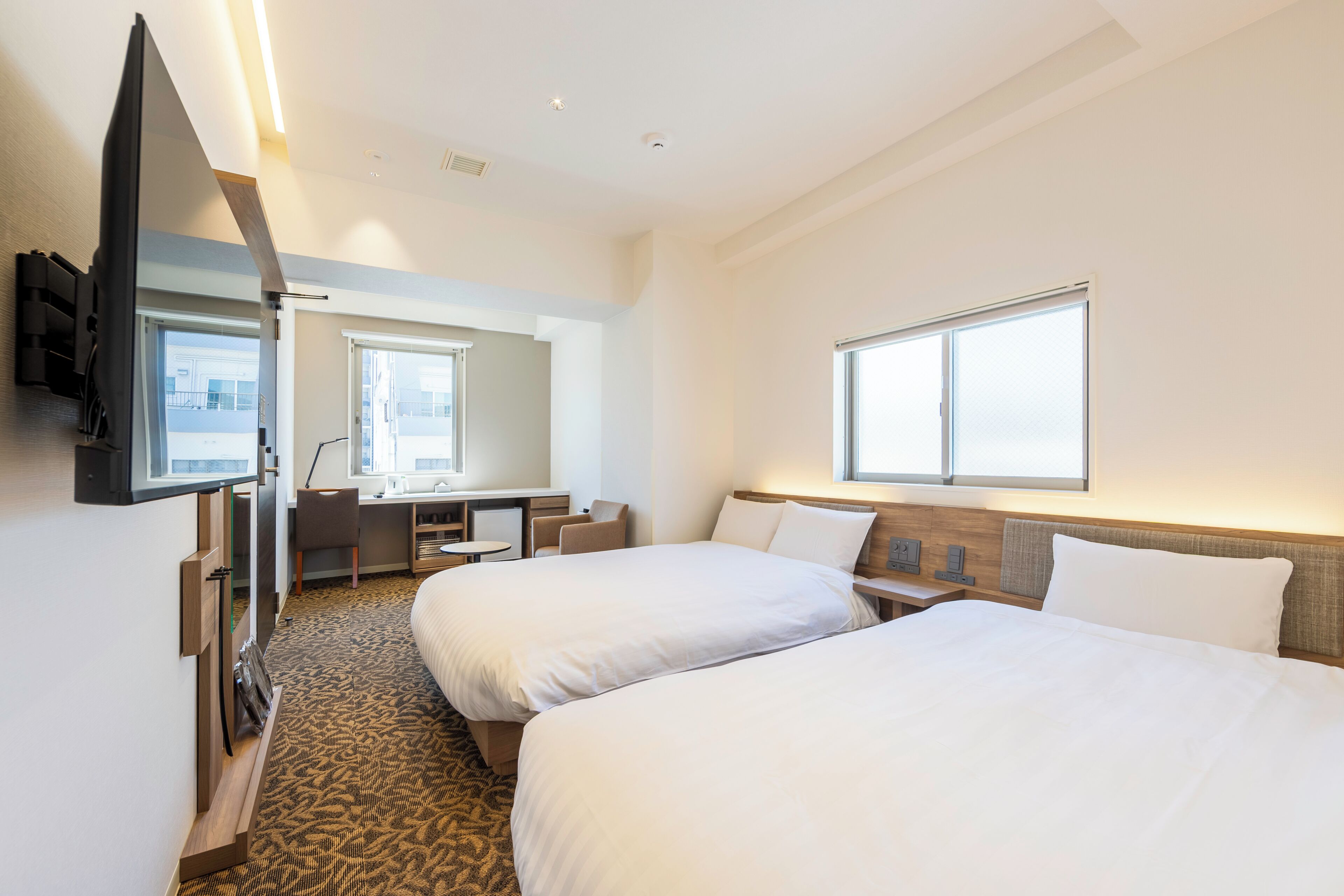 Habitación de hotel con dos camas, un escritorio, una silla, un televisor y una ventana.