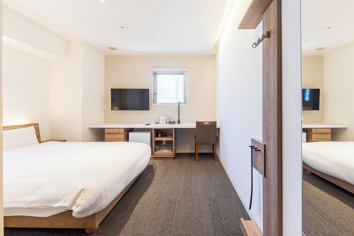Ein Hotelzimmer mit Bett, Schreibtisch, Stuhl, Fernseher und Spiegel.