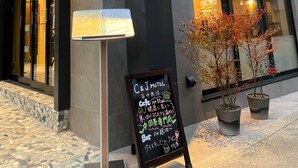 L’extérieur d’un hôtel, avec une enseigne bien visible, un menu écrit à la craie et des plantes en pot.