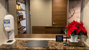 Un comptoir d’accueil avec une horloge numérique, un panneau indiquant la réception, et une plante en pot ornée de fleurs rouges.