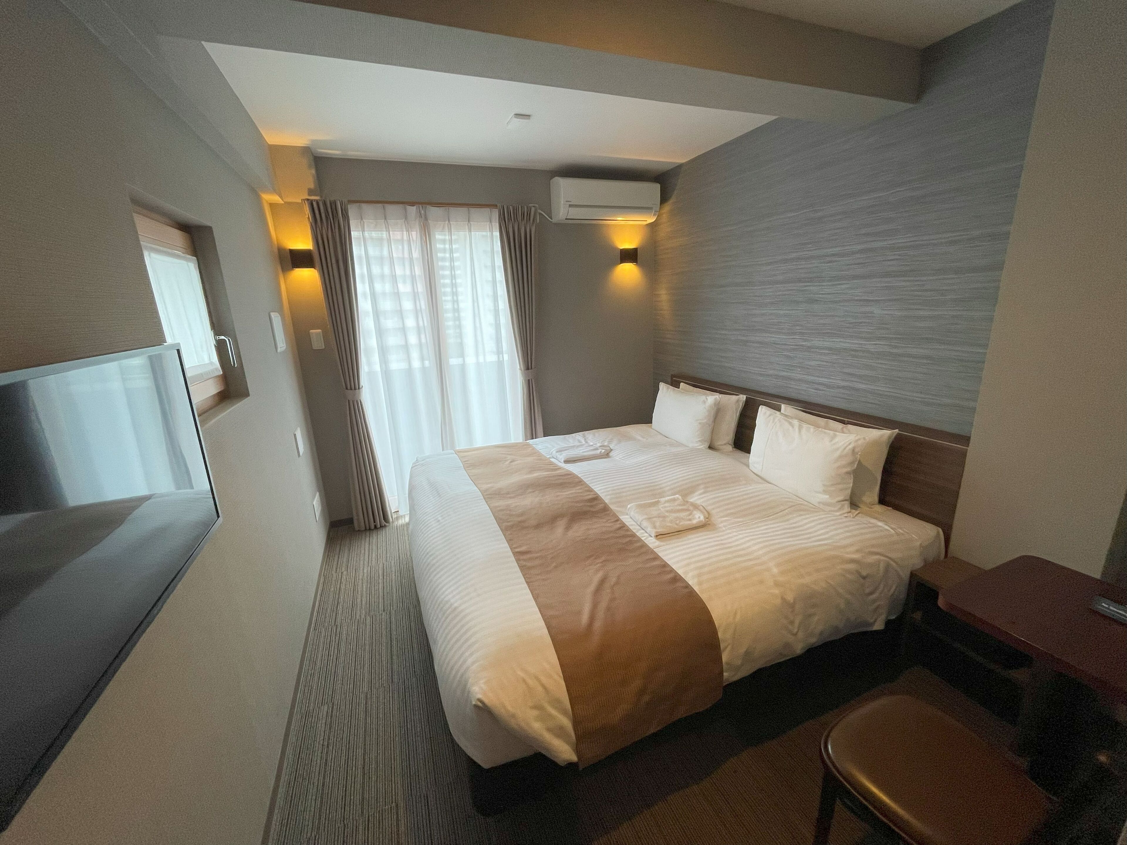 Ein Hotelzimmer mit einem großen Bett, einem Schreibtisch, einem Fernseher und einem Fenster mit Vorhängen.