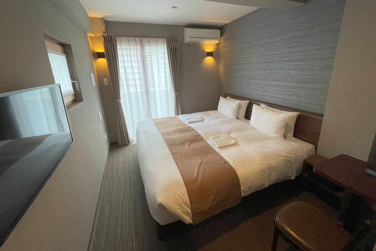 A hotel room with a large bed, a desk, a TV, and a window with curtains.