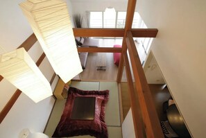 Une pièce avec un plafond en pente, un plancher en bois, un tapis rouge, un lit, une fenêtre et un canapé.