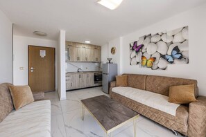 A living room with a sofa, a coffee table, and a kitchen in the background. - Sea View Apartment | Durrës Waterfront by PikHost (Durrës)