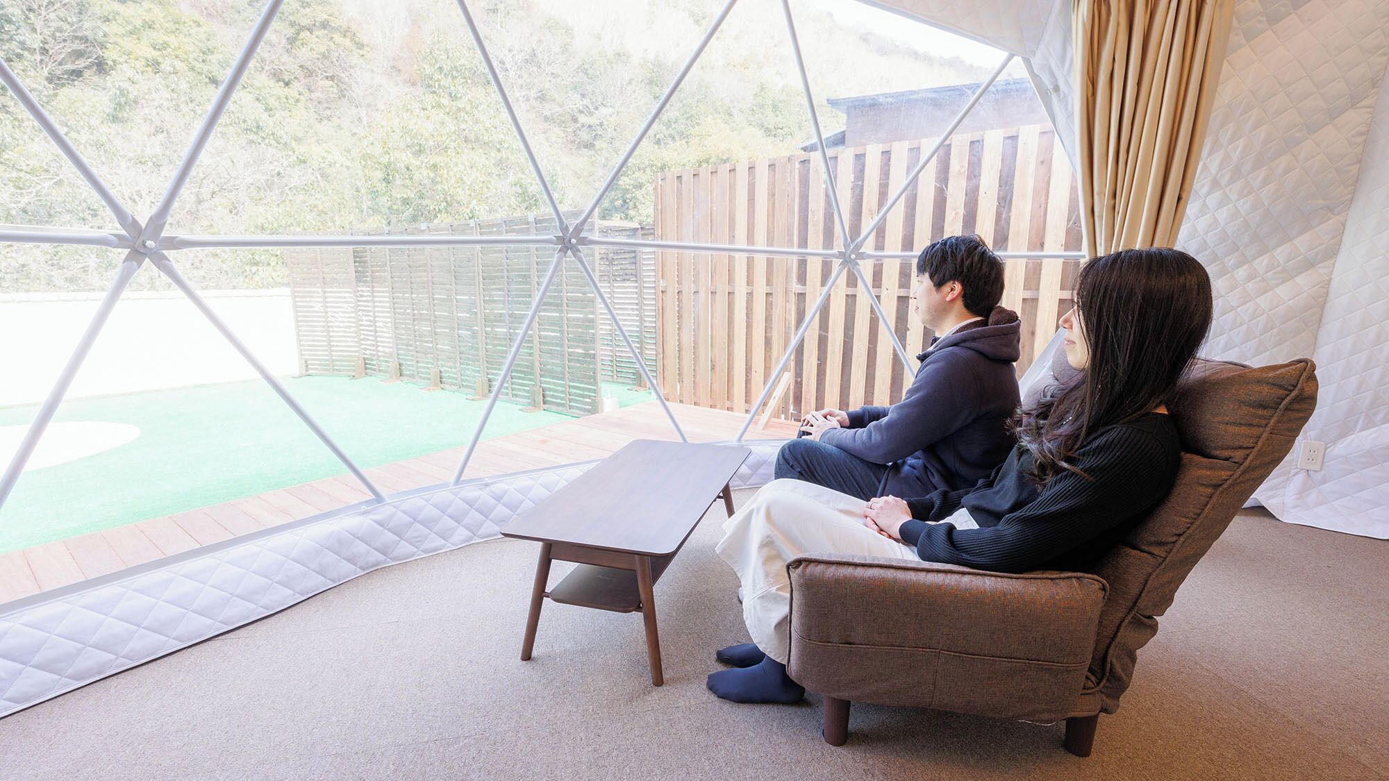 A room with a geometric glass enclosure, a cushioned seating area, and a small table.