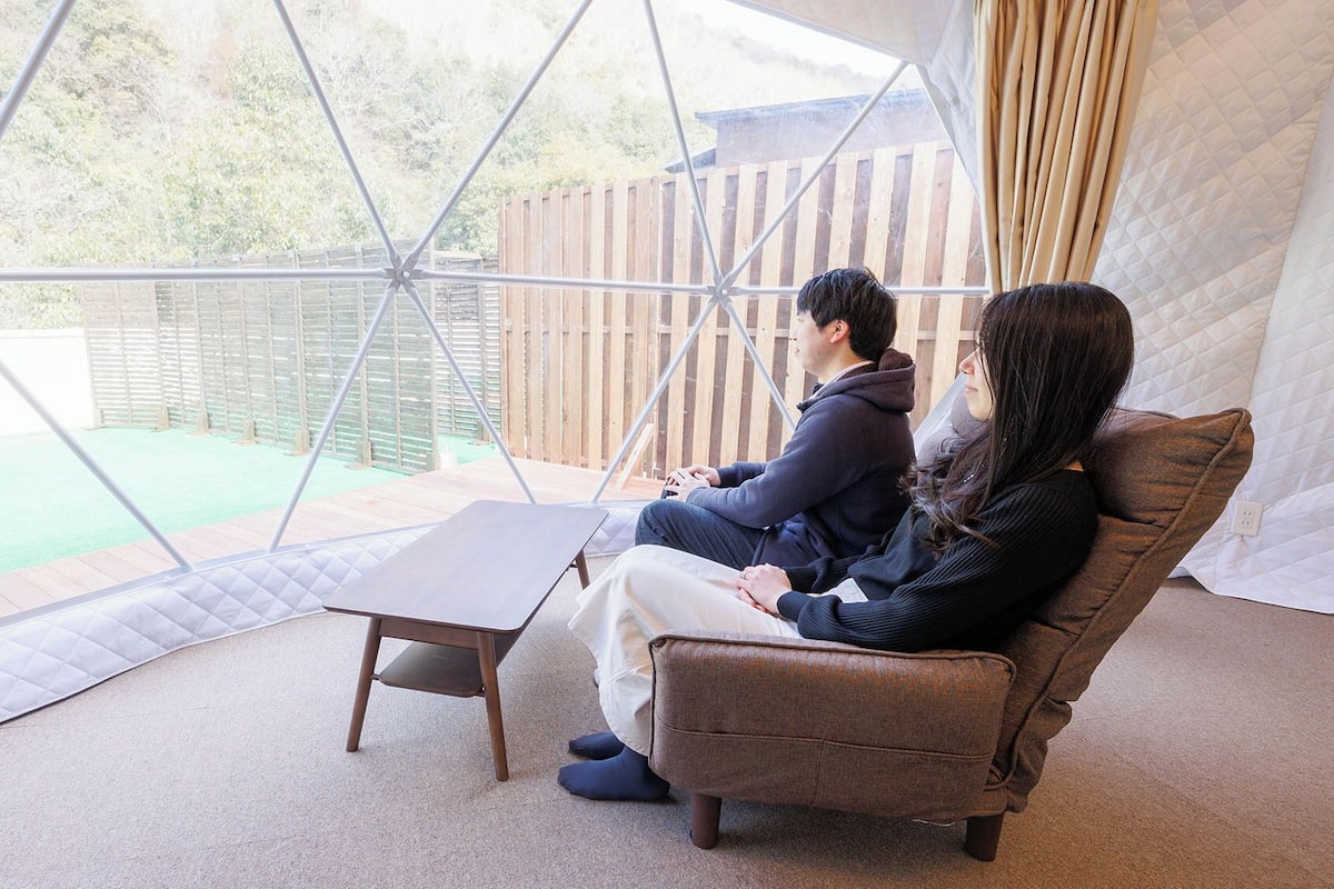 A room with a geometric glass enclosure, a cushioned seating area, and a small table.
