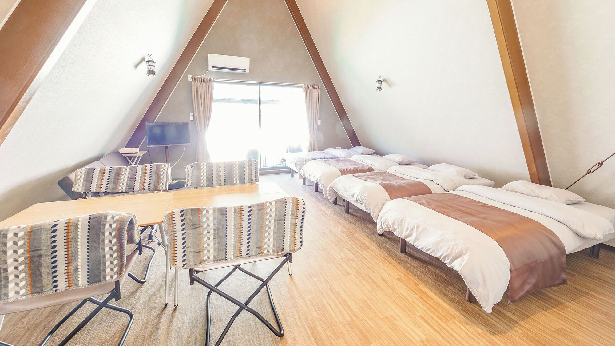 A triangular room with a long table and multiple beds.
