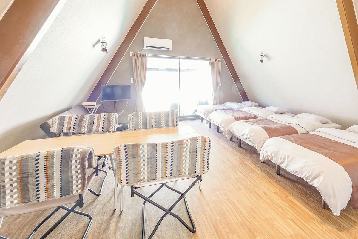 A triangular room with a long table and multiple beds.