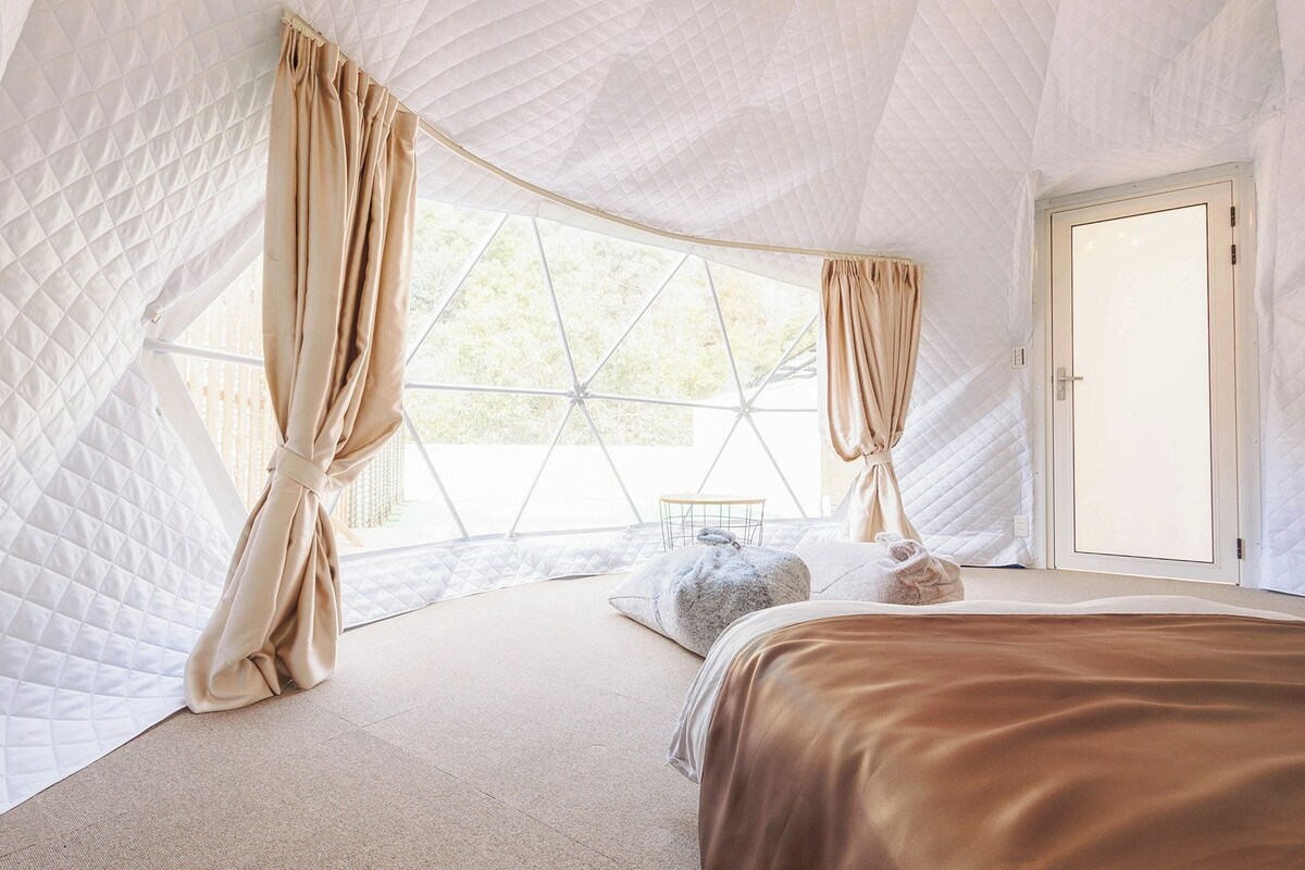 A tent-style room with a bed, curtains, and a view through a large window.