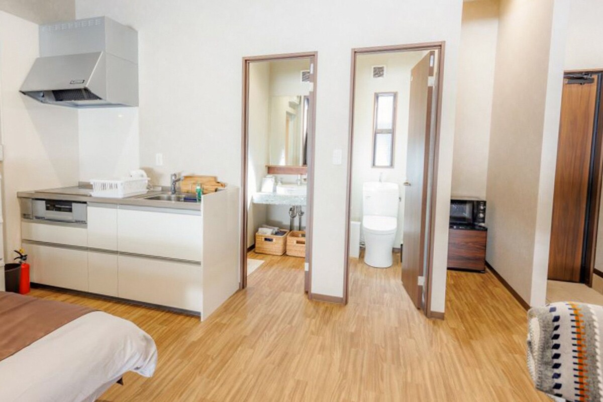 A hotel room with a bed, kitchenette, and a bathroom visible through an open door.