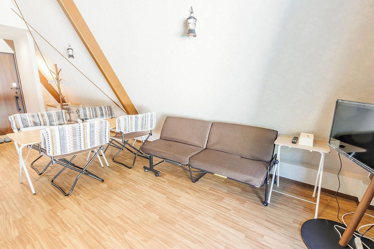 A modern living room with a sofa, a dining table with chairs, a TV, and a lamp.