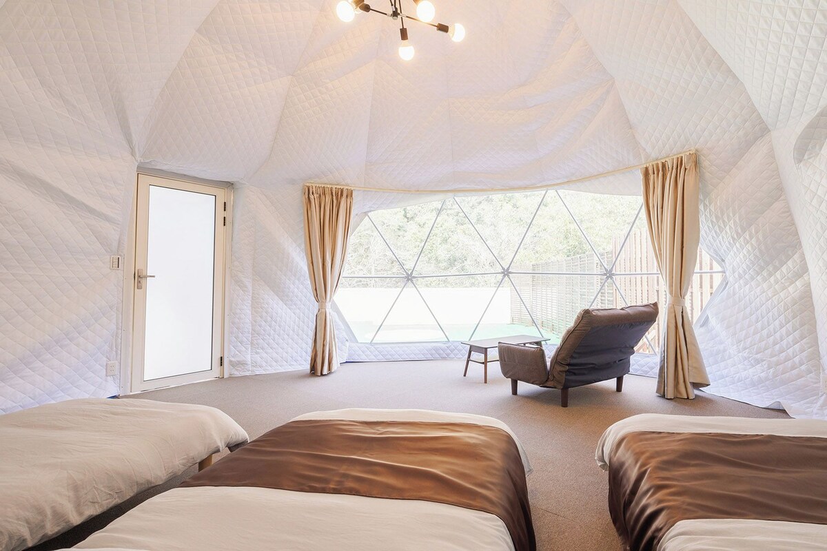 A tent-style room with two beds, a table, and chairs, and a view through the window.
