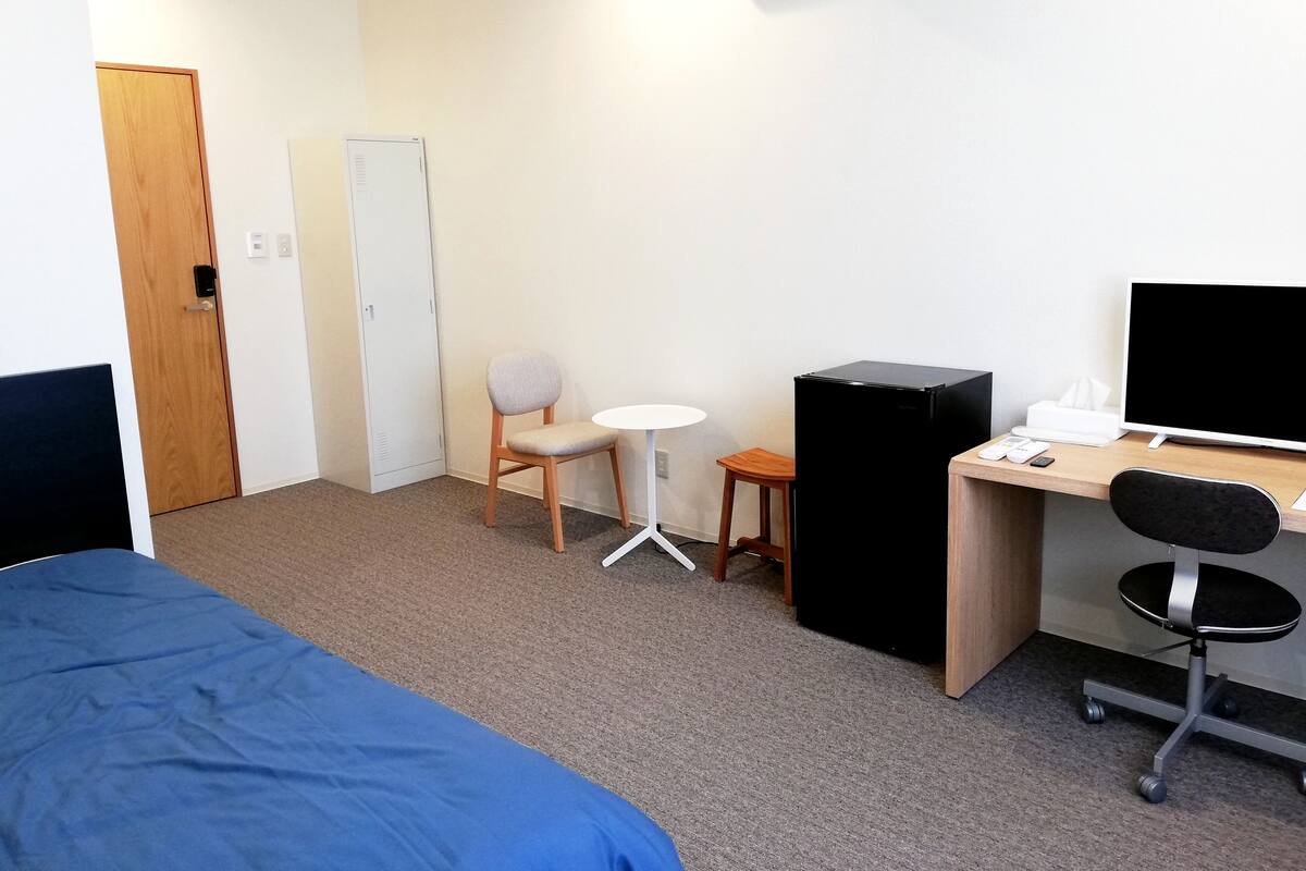 Ein Hotelzimmer mit einem Bett, einem Schreibtisch mit Computer, einem Stuhl, einem kleinen Tisch und einem Kleiderschrank.