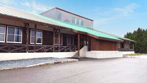 En toetagers bygning med et grønt tag, træfacade og en overdækket veranda med trapper til indgangen.
