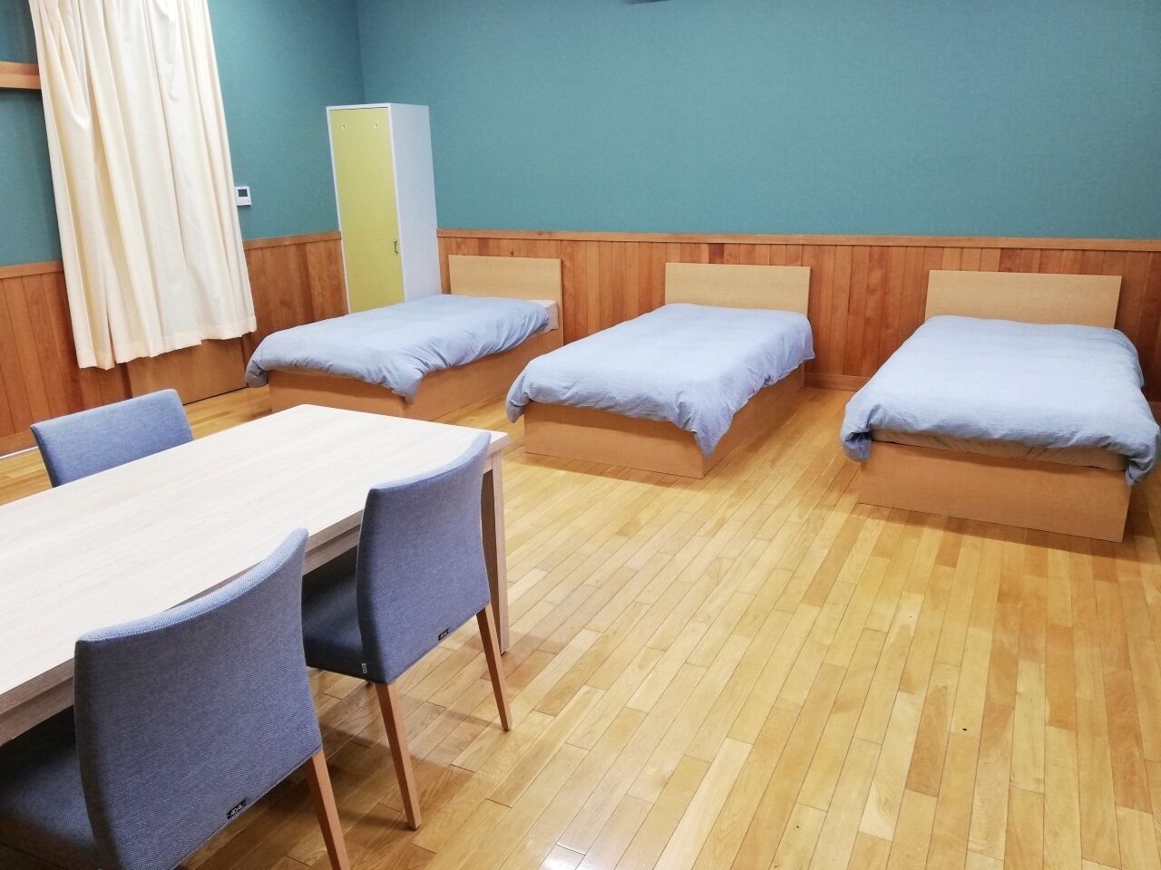 Une chambre avec quatre lits simples, une table en bois avec des chaises et une armoire.