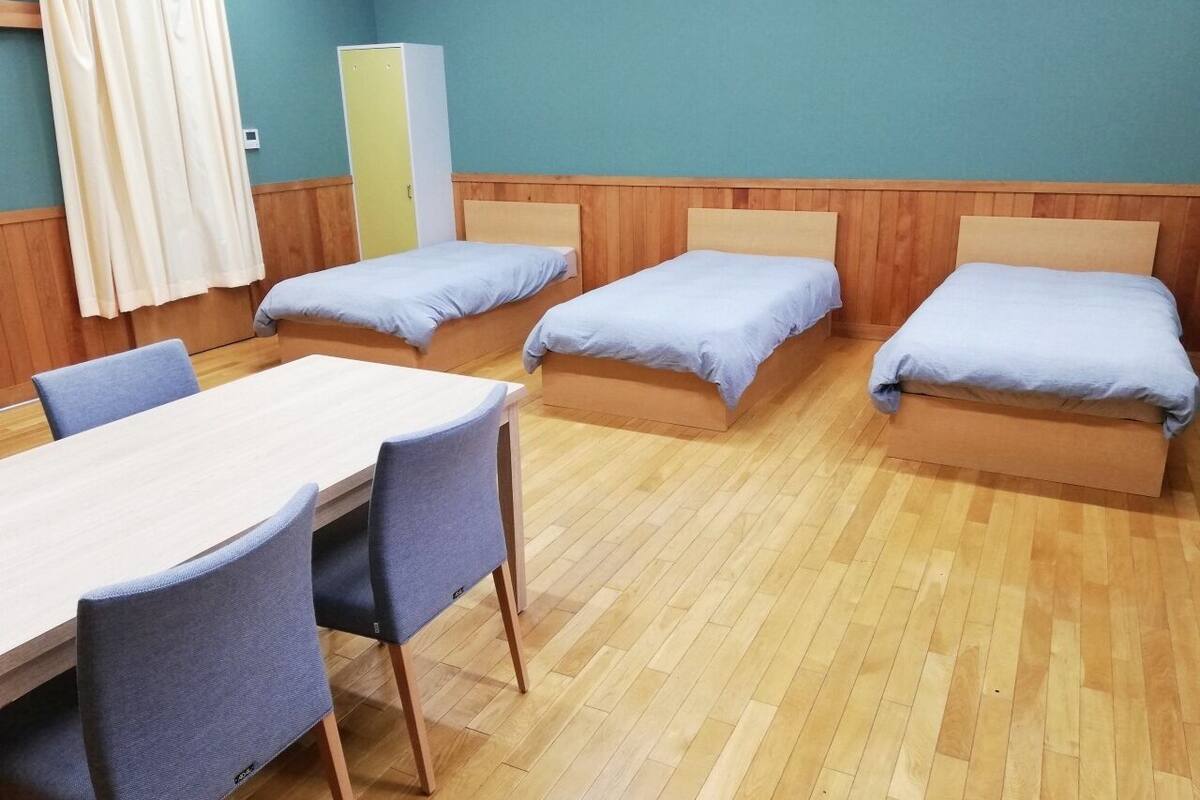 Ein Zimmer mit vier Einzelbetten, einem Holztisch mit Stühlen und einem Kleiderschrank.