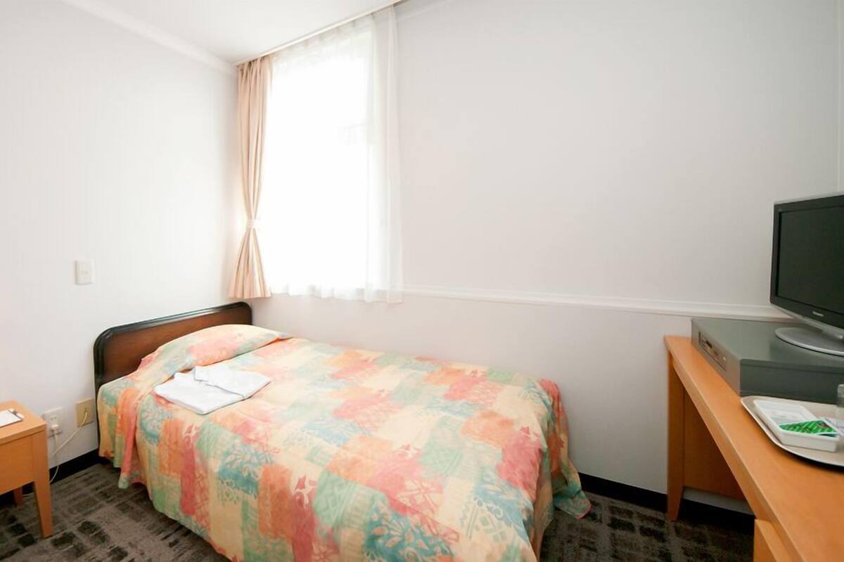 A hotel room with a bed, a desk with a television, a lamp, and a telephone.